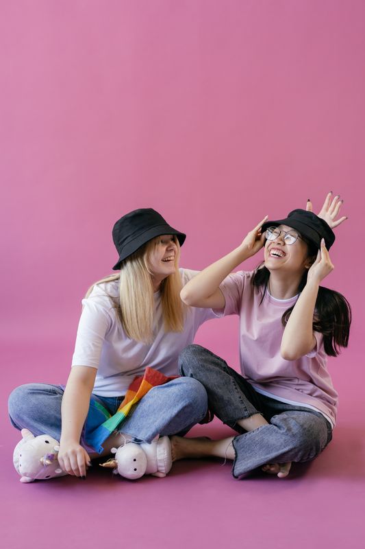 Two people sitting on the floor wearing similar bucket hats and laughing together