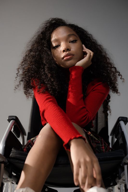 Person wearing red dress sitting in a wheelchair, looking pensive